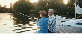 Großvater mit Enkel am See beim Angeln im Sonnenuntergang.