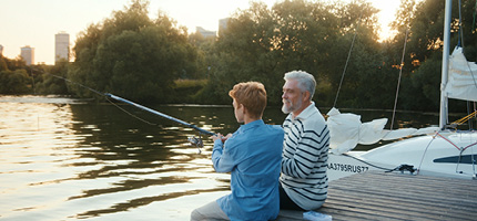 Großvater mit Enkel am See beim Angeln im Sonnenuntergang.