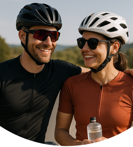 Mann und Frau stehen mit ihren Fahrrädern, Fahrradhelmen und Sportsonnenbrillen am Straßenrand und machen Pause. Dabei lächeln sie.